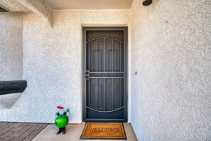 A door with a metal gate, a welcome mat, and a small green figurine on the ground. - Pool + Spa Retreat | Game Garage | Trailer Parking (Lake Havasu City)