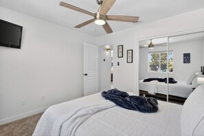 Une chambre à coucher comprenant un lit, un ventilateur de plafond, un grand miroir et un téléviseur fixé au mur.