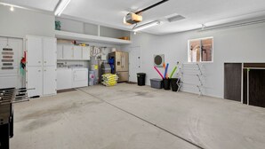 Ett rent och väl upplyst garage med vita väggar, ett stort arbetsbord och diverse verktyg och utrustning.