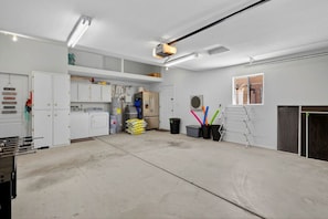 A clean, well-lit garage with white walls, a large workbench, and various tools and equipment. - Pool + Spa Retreat | Game Garage | Trailer Parking (Lake Havasu City)