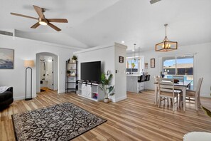 A modern living room with a flat-screen TV, a ceiling fan, and a dining area with a view of the outdoors. - Pool + Spa Retreat | Game Garage | Trailer Parking (Lake Havasu City)