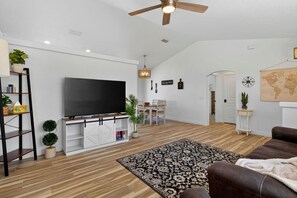 Un salon spacieux doté d’un téléviseur à écran plat, de parquet, d’un tapis à motifs et d’un ventilateur de plafond.