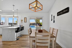 A modern kitchen with a marble island, wooden dining table, and pendant lighting. - Pool + Spa Retreat | Game Garage | Trailer Parking (Lake Havasu City)