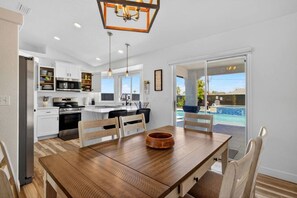 A modern kitchen with a dining area, a large island, and a view of a swimming pool. - Pool + Spa Retreat | Game Garage | Trailer Parking (Lake Havasu City)