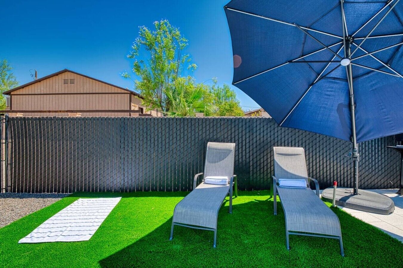 Ein Garten mit Kunstgrashalm, zwei Liegestühlen und einem großen Sonnenschirm.