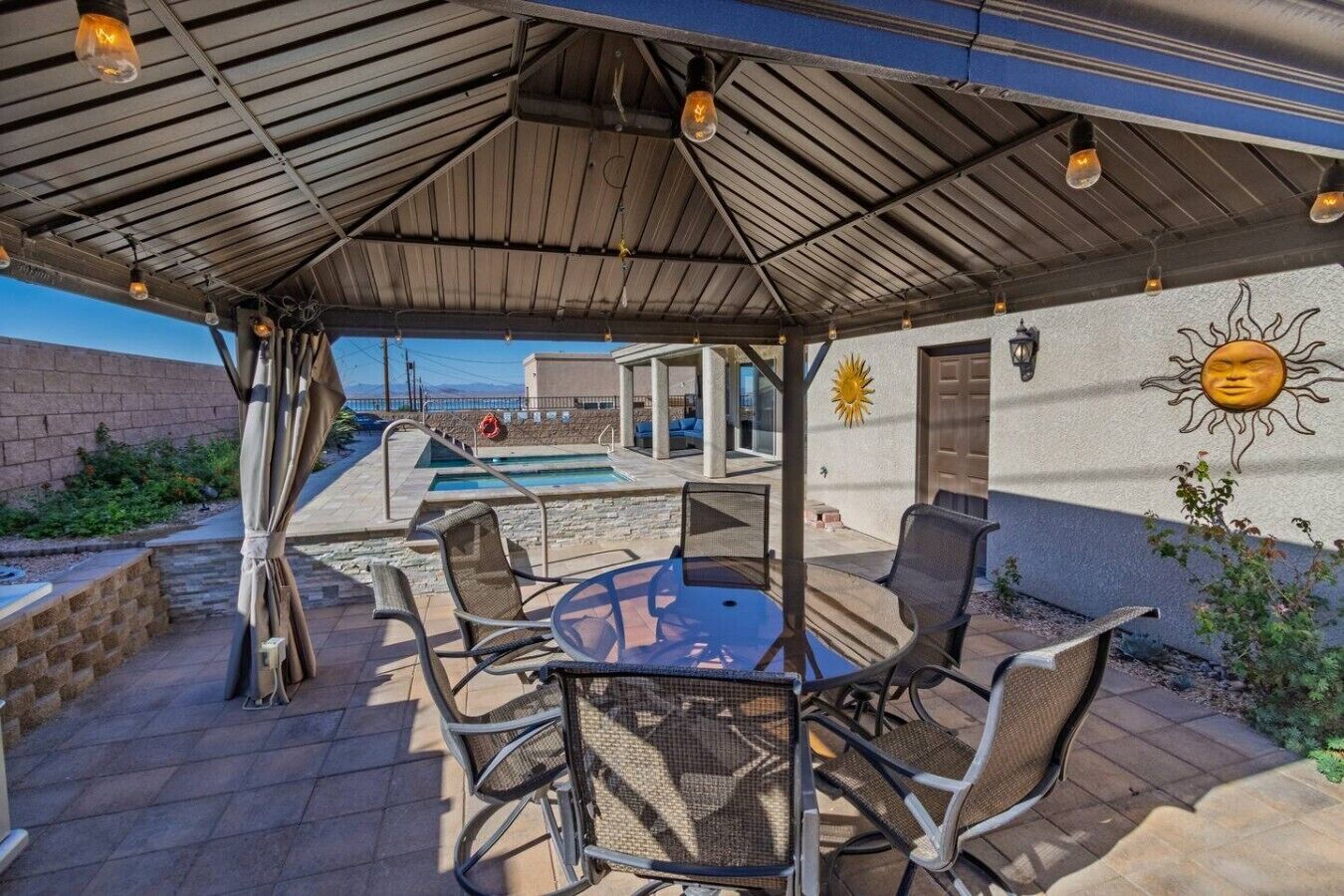 An outdoor patio with a pool, seating area, and a covered section with a view of the pool.