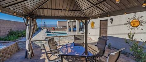 An outdoor patio with a pool, seating area, and a covered section with a view of the pool.
