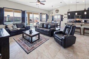 A spacious living room with leather sofas, a coffee table, and a kitchen area with modern appliances. - Pool, Spa & 100” TV | Near Windsor (Lake Havasu City)