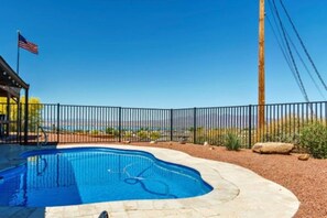 En swimmingpool med en buet kant, omgivet af et hegn i sort metal, og et amerikansk flag på en flagstang.
