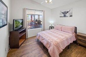 A bedroom with a bed, a television, a window with a view, and a wall-mounted artwork. - Pet-Friendly | Sunset View Deck | Pool & Spa (Lake Havasu City)