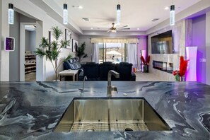 Ein modernes Wohnzimmer mit einer schwarzen Ledersofa, einem Essbereich mit Tisch und Stühlen, einer Küche mit Marmorarbeitsplatte und Spüle sowie einem Deckenventilator.