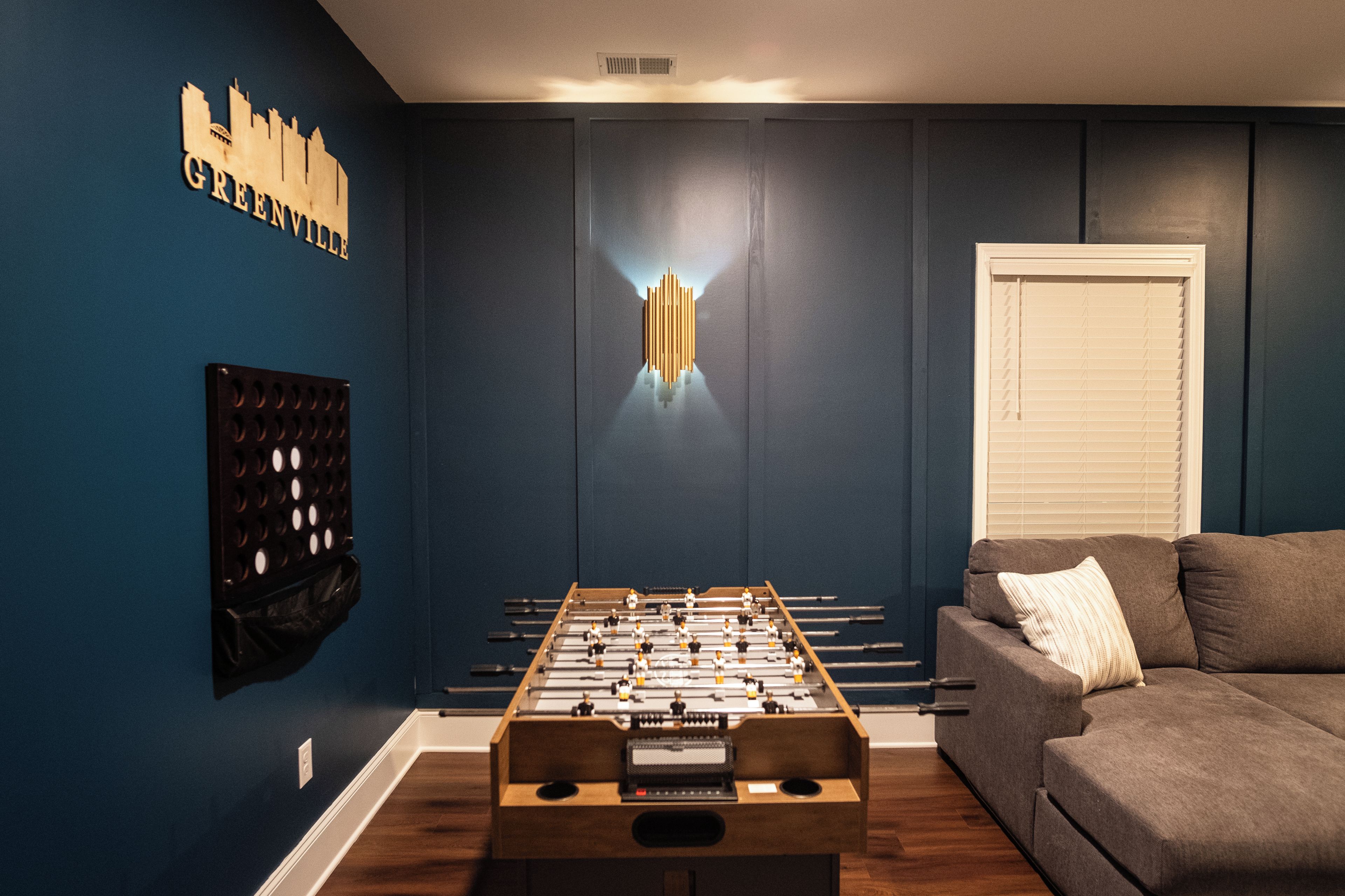 Una habitación con mesa de futbolín, sofá y lámpara fijada en la pared.