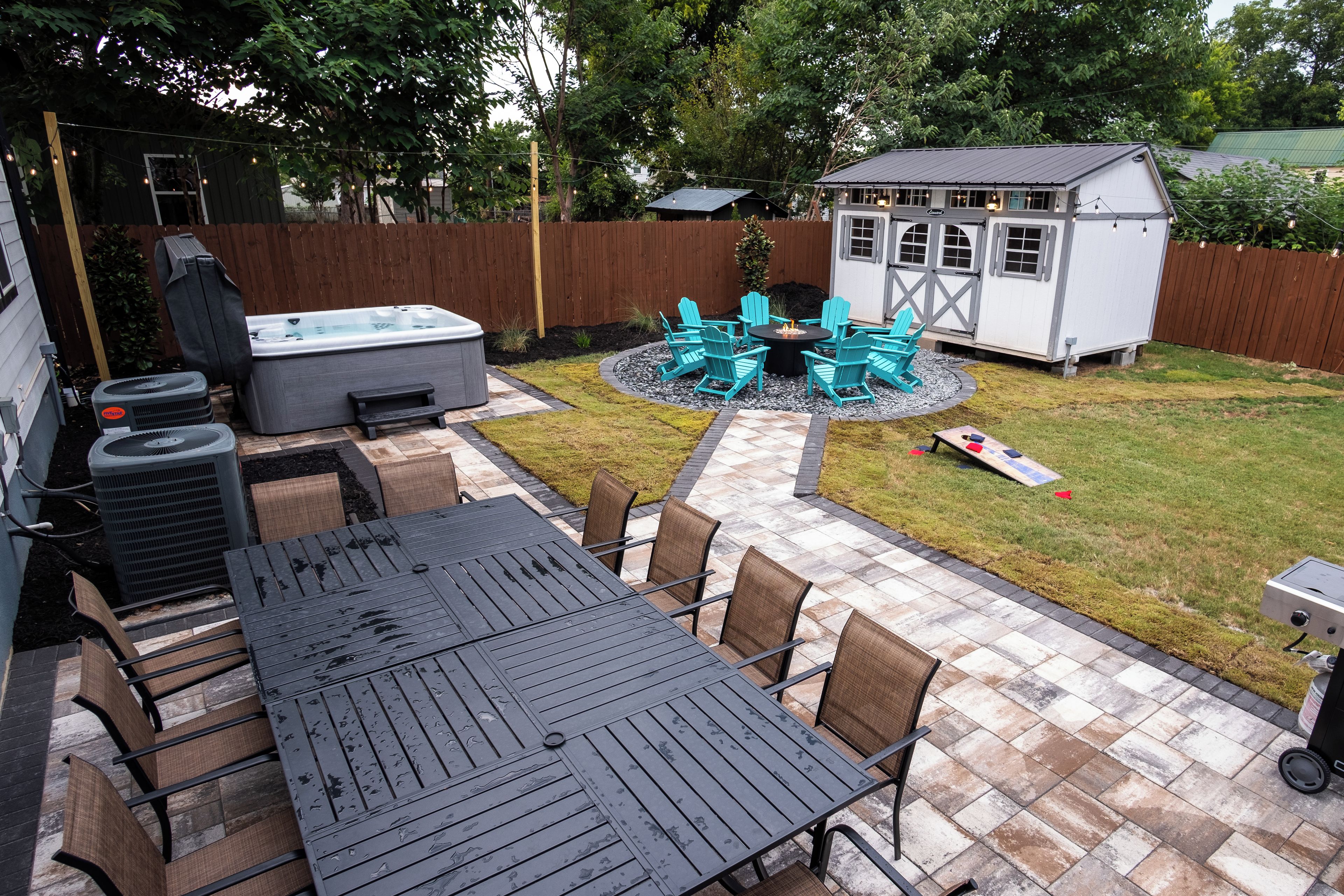 Ein Garten mit einer Terrasse, einem Tisch und Stühlen, einem Whirlpool und einem kleinen Gartenhaus.
