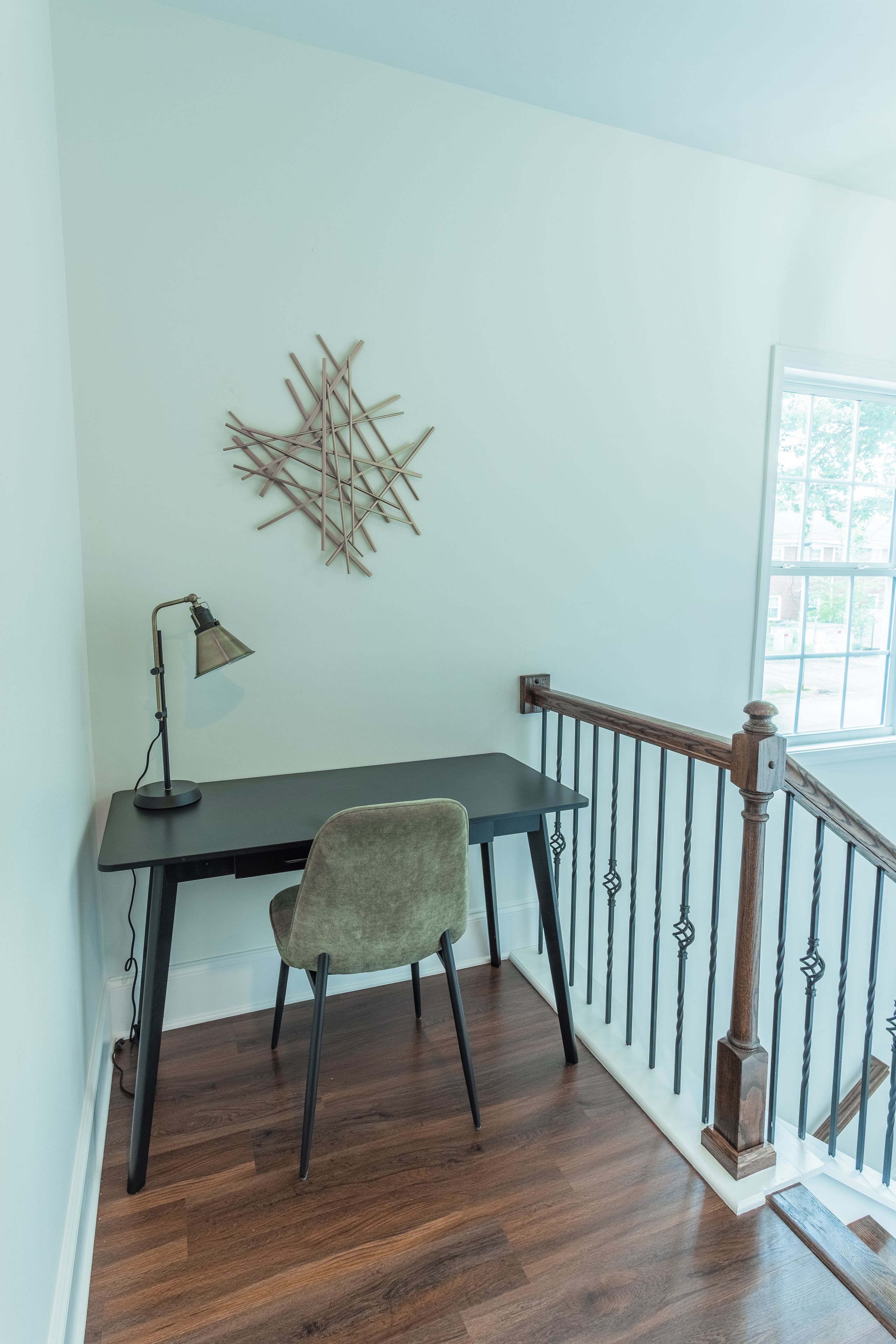 Habitación de esquina con escritorio, silla, lámpara y un adorno de pared.