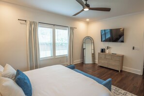 Ein Schlafzimmer mit Bett, Kommode, Spiegel, Deckenventilator und einem Fenster mit Vorhängen.