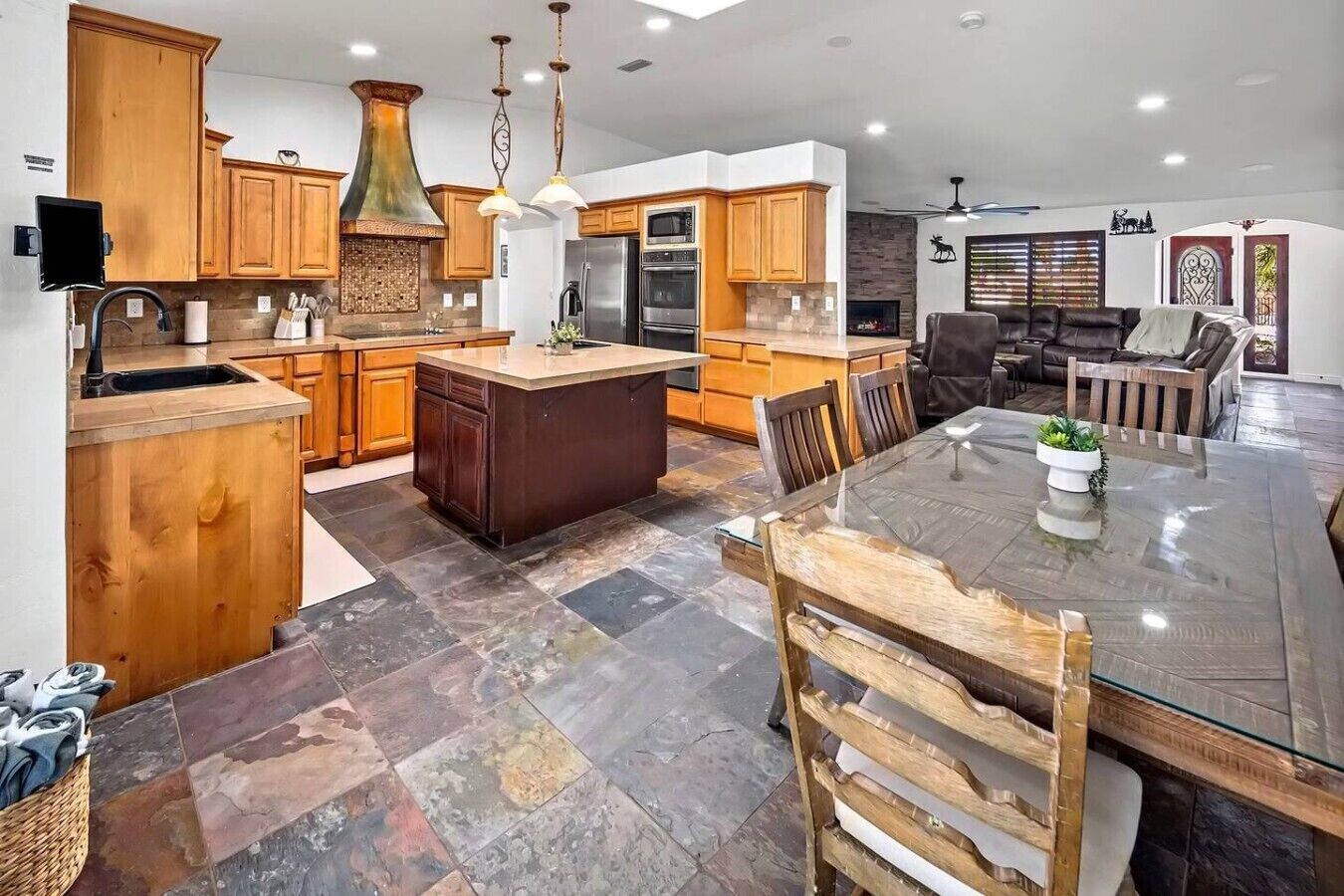 A modern kitchen with wooden cabinets, a central island, and a dining area with a glass table.