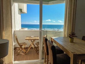 Ein Balkon mit Holztisch und -stühlen, einer Topfpflanze und Blick auf das Meer.