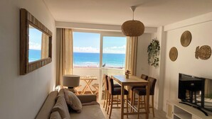 Una sala de estar con sofá, mesa de comedor, sillas, televisor y vista al océano.