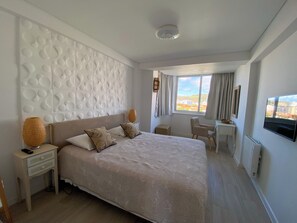 A modern hotel room with a large bed, a desk, and a view of the city. - Sea View Apartment - Right on the Beach in Costa da Caparica (Costa de Caparica)