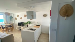 Una cocina moderna con una isla central, un comedor con mesa y sillas, y vista al mar a través de una ventana.