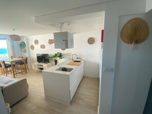 A modern kitchen with a central island, a dining area with a table and chairs, and a view of the sea through a window. - Sea View Apartment - Right on the Beach in Costa da Caparica (Costa de Caparica)