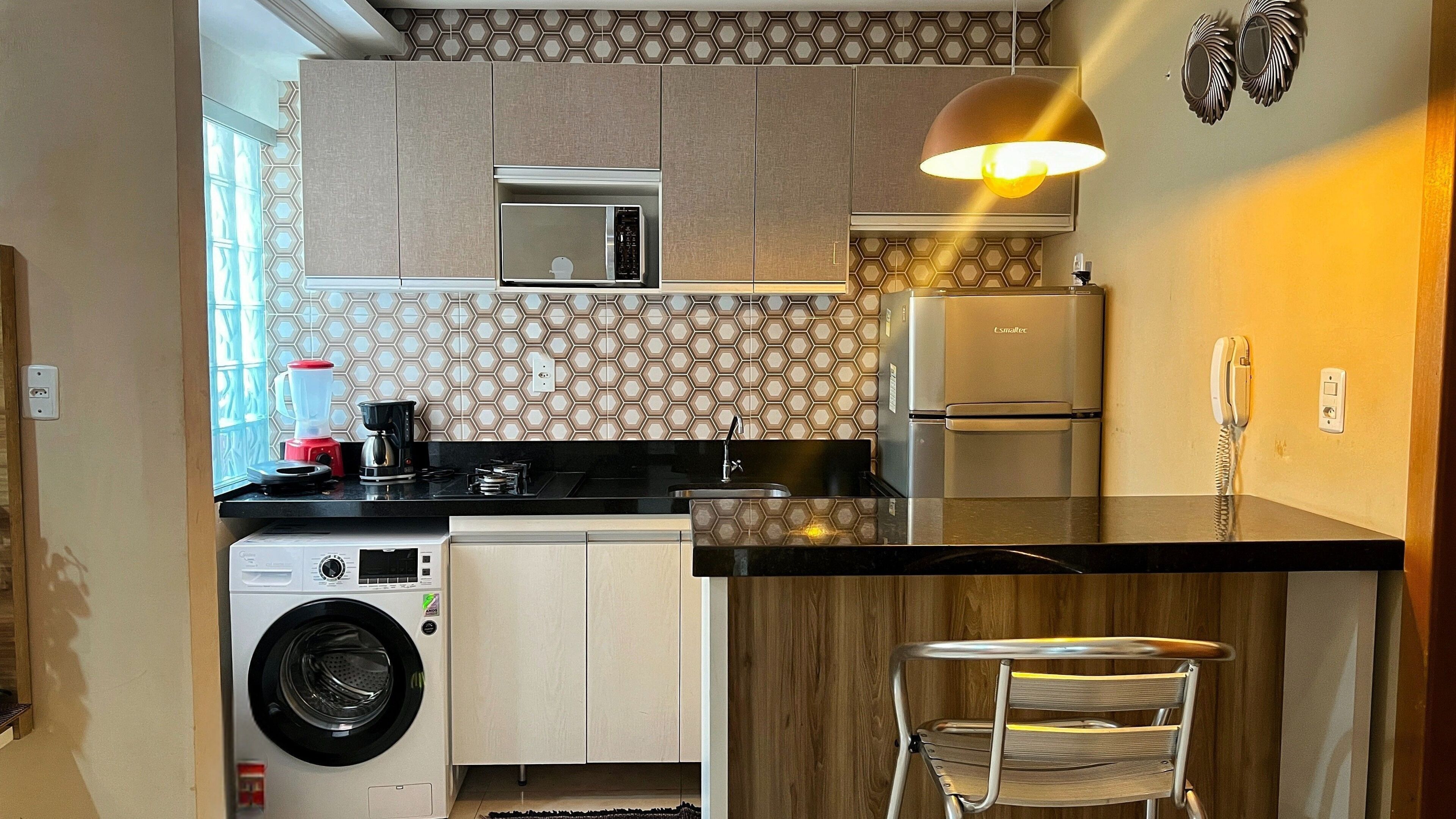 A compact kitchen with a washing machine, a microwave, a coffee maker, and a refrigerator.