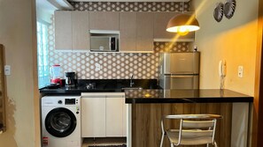 A compact kitchen with a washing machine, a microwave, a coffee maker, and a refrigerator. - Apto 101 (Belém)