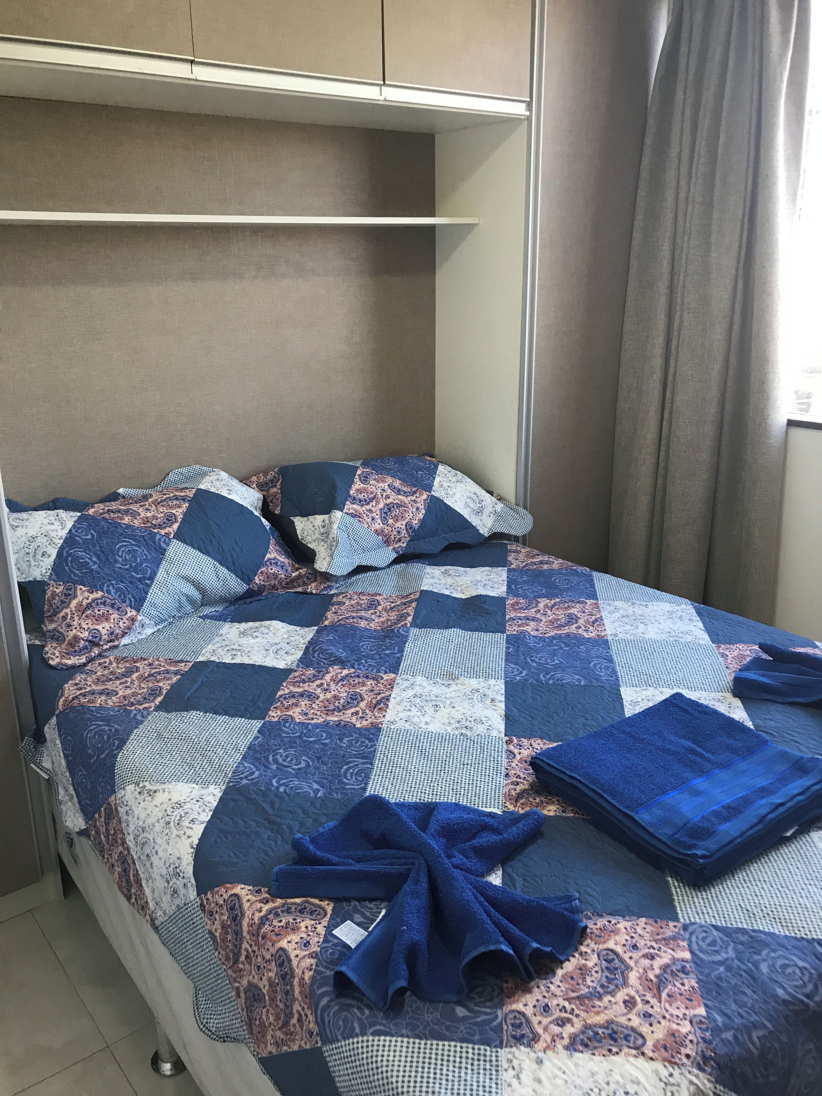 A bed with a blue and white quilt, a folded blue blanket, and a pillow with a paisley pattern.