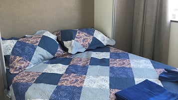 Ein Bett mit einer blau-weißen Steude, einer gefalteten blauen Decke und einem Kissen mit Paisley-Muster.