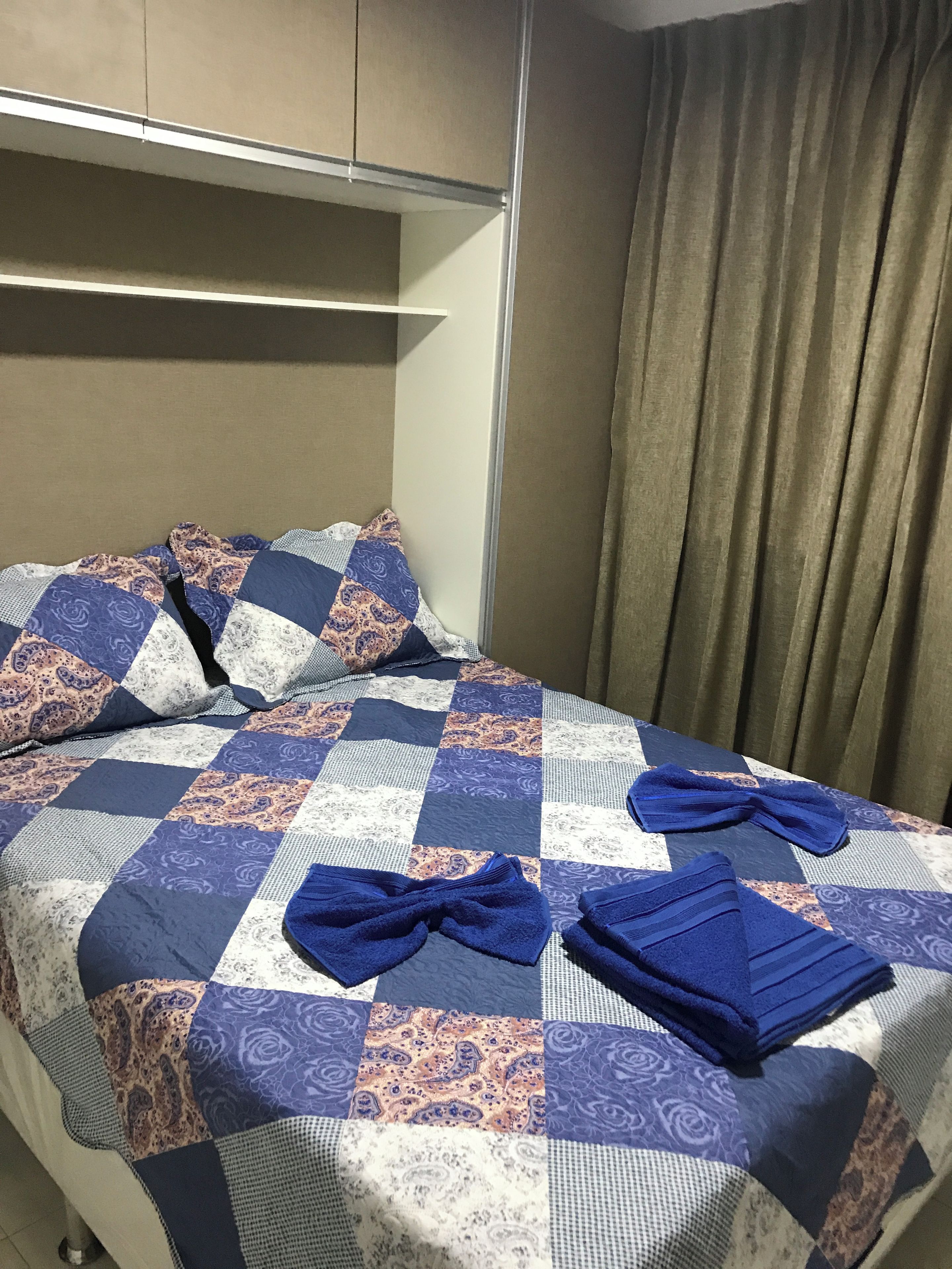 A hotel room with a bed, pillows, a quilt, and a curtain.