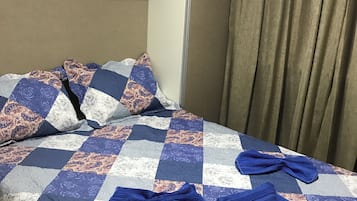 A hotel room with a bed, pillows, a quilt, and a curtain.