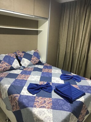 Ein Hotelzimmer mit einem Bett, Kissen, einer Tagesdecke und einem Vorhang.