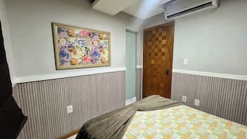 A bedroom with a bed, a wall-mounted air conditioner, a door, and a framed floral artwork.