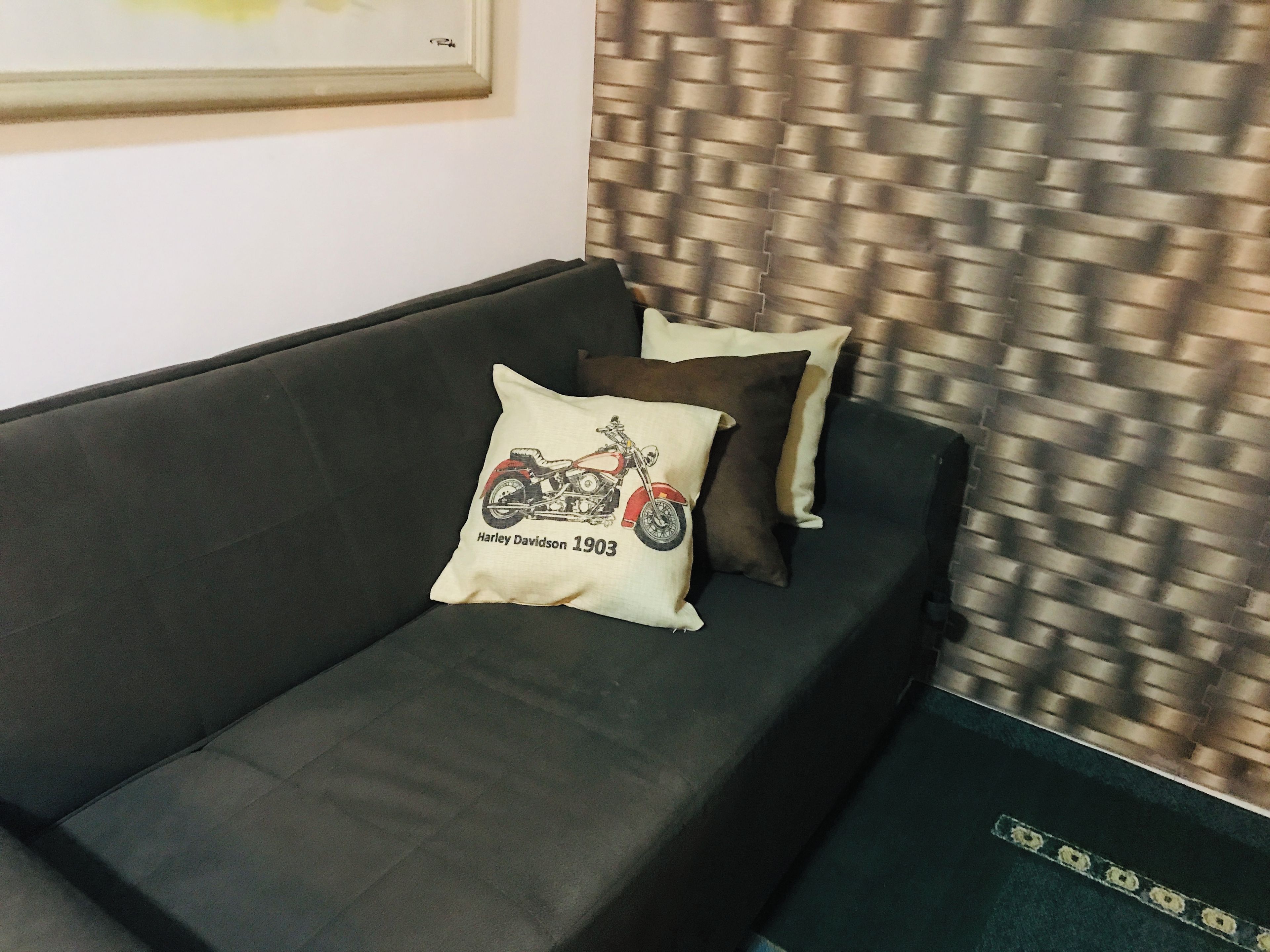 A dark-colored sofa with a pillow featuring a motorcycle design and the year 1903.