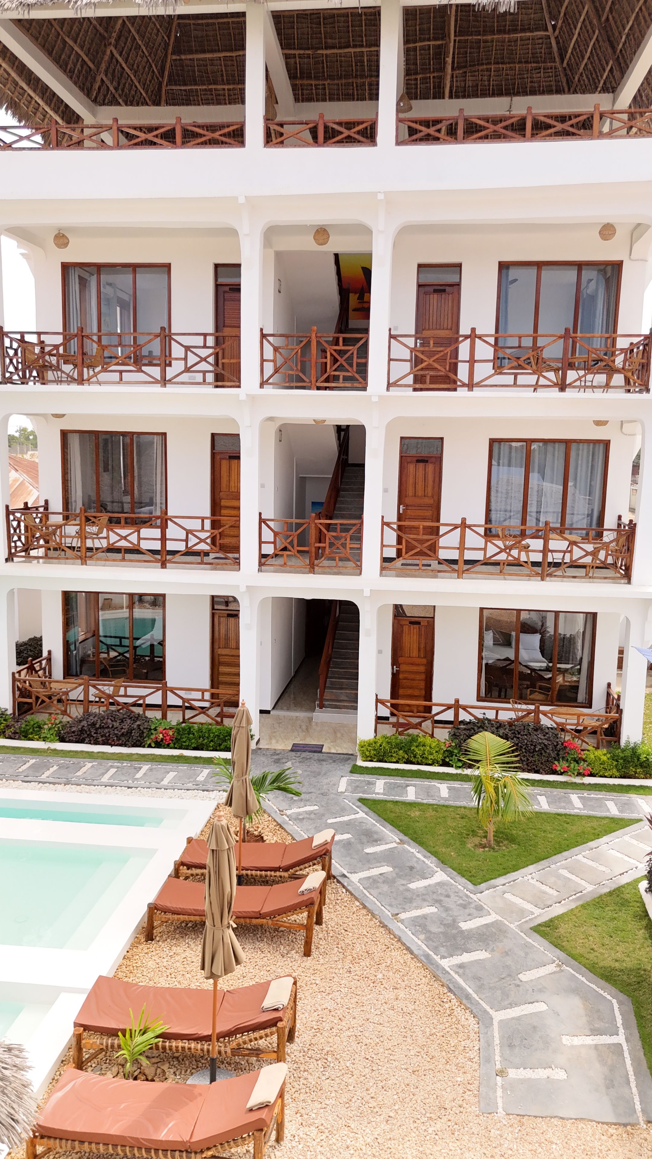 Un hotel de varios pisos con balcones, piscina y mobiliario exterior.