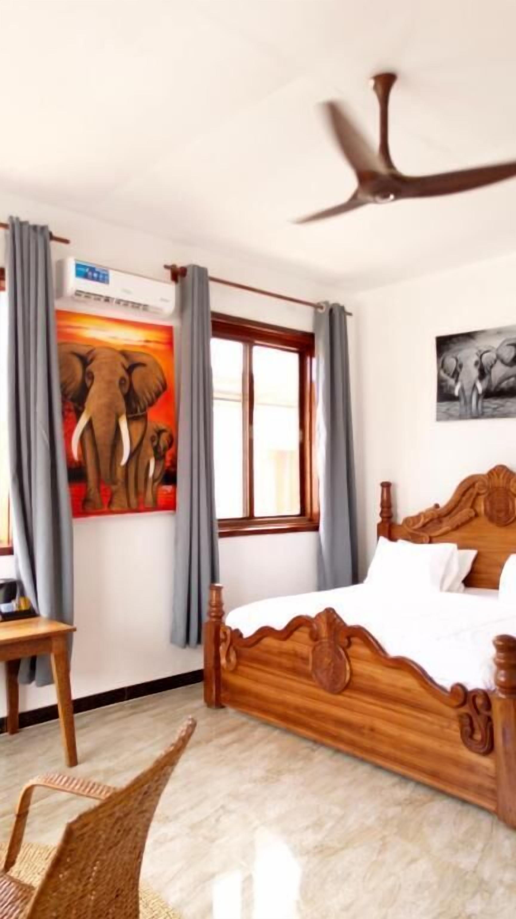A bedroom with a wooden bed, a ceiling fan, a window with curtains, and a wall-mounted air conditioner.