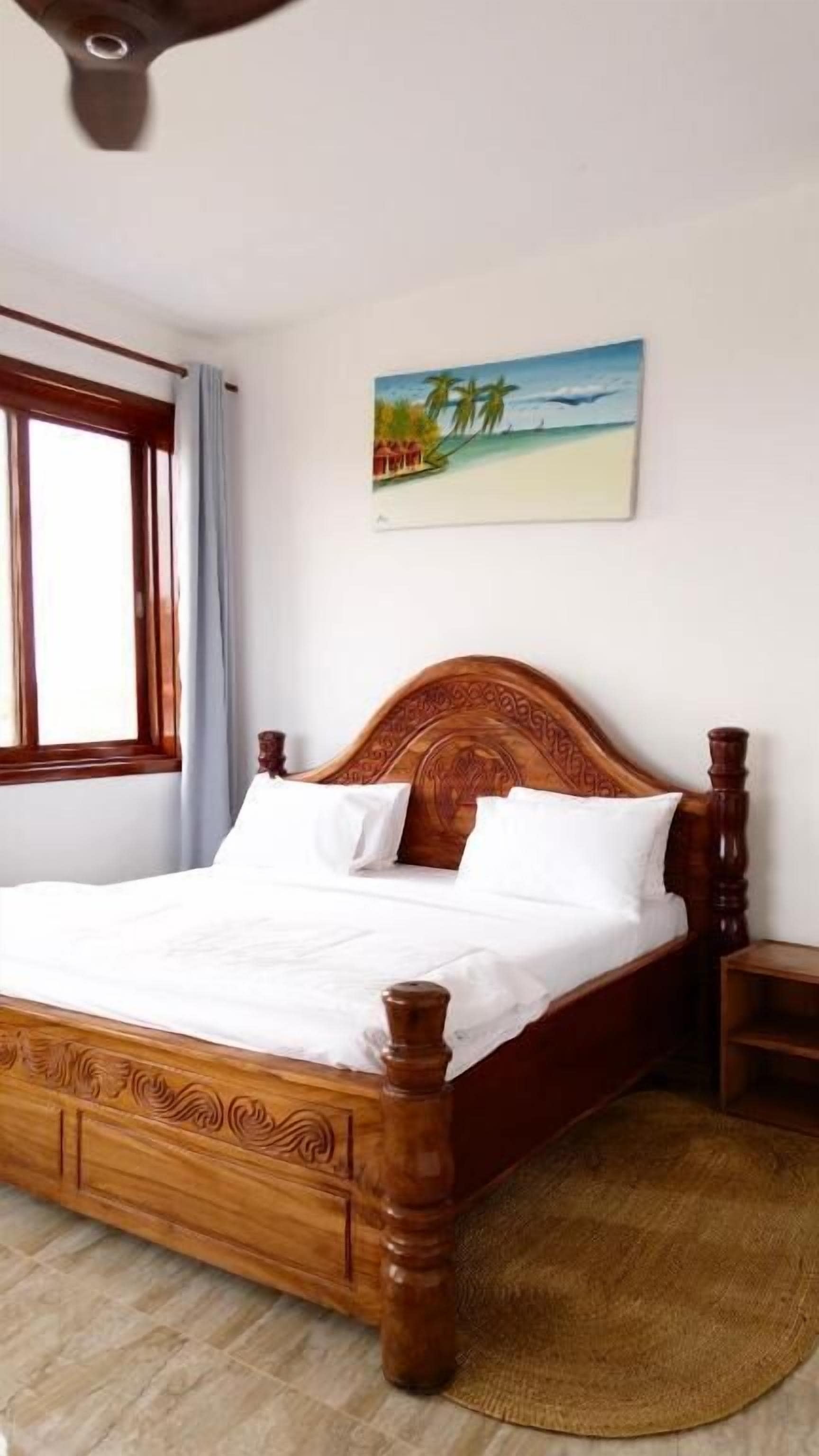 A wooden bed with white linens in a room with a beach-themed painting on the wall.