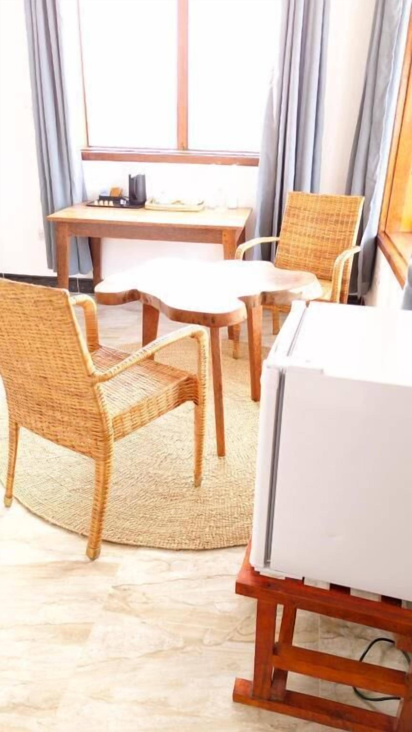 A room with a dining table, four wicker chairs, a whiteboard, and a television on a wooden stand.