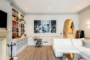 Un salon avec un canapé blanc, une bibliothèque, une cheminée et un grand tableau en noir et blanc.