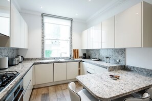 Una cocina moderna con armarios blancos, encimeras de granito y un amplio ventanal.