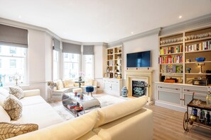 Ein geräumiges Wohnzimmer mit einer großen Couch, einem Couchtisch und einem Kamin. Ein Bücherregal ist mit Büchern und Dekoration gefüllt.
