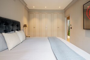Ein Schlafzimmer mit einem großen Bett, einem Kopfteil, einem Nachttisch, einer Lampe, einem Kleiderschrank und einem Spiegel.