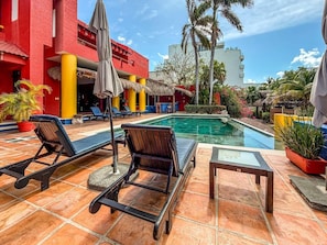A poolside area with lounge chairs, a small table, and a thatched-roof structure. - Junior Suite Garden View at Casa de los Suenos (Isla Mujeres)