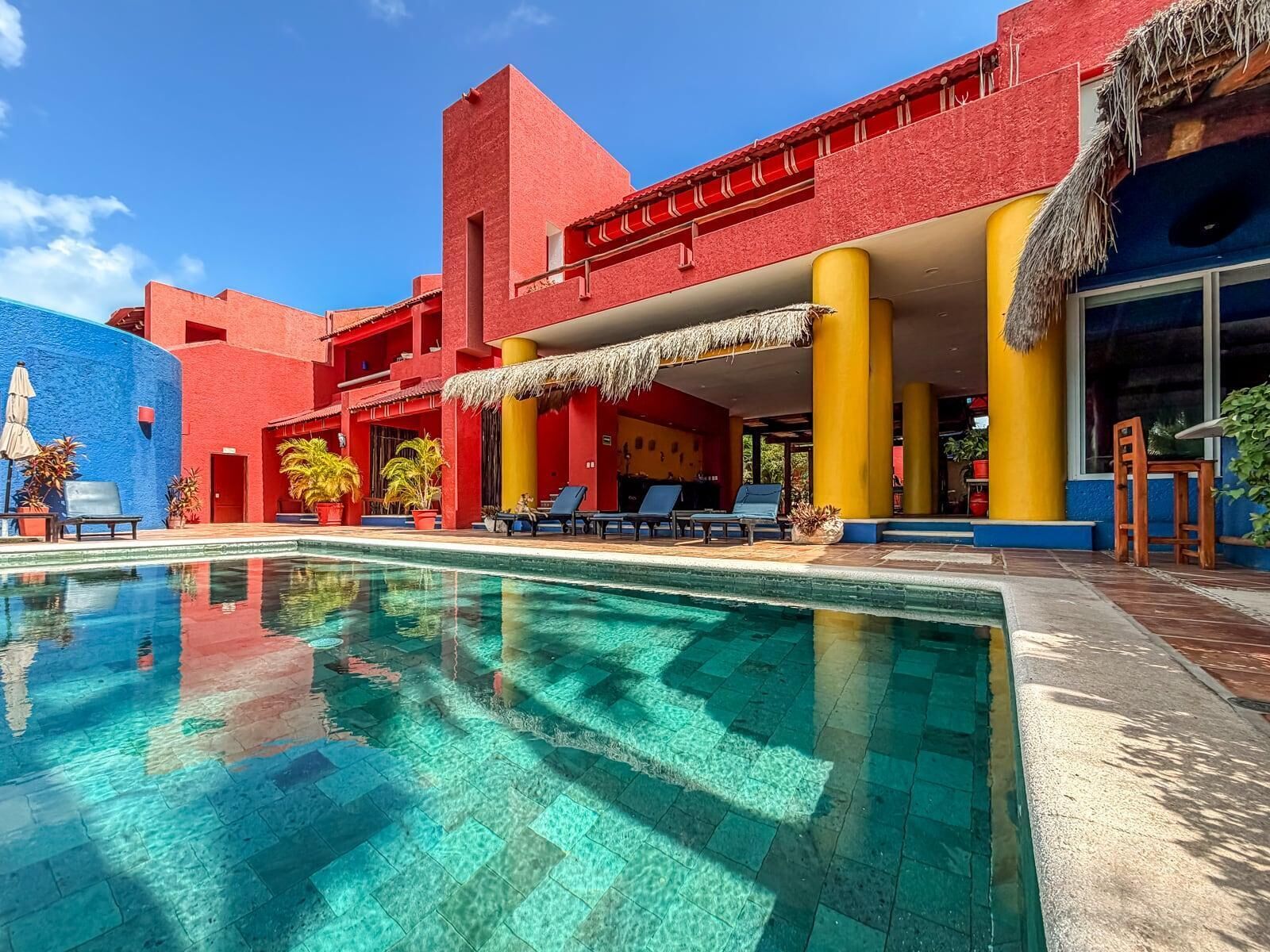 A poolside area with a clear pool, lounge chairs, and a building with red and yellow walls.