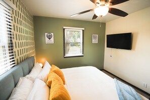 A bedroom with a bed, a ceiling fan, a window with blinds, and a wall-mounted television. - Hot Tub_Theater_Game Room_Poker Table (Omaha)