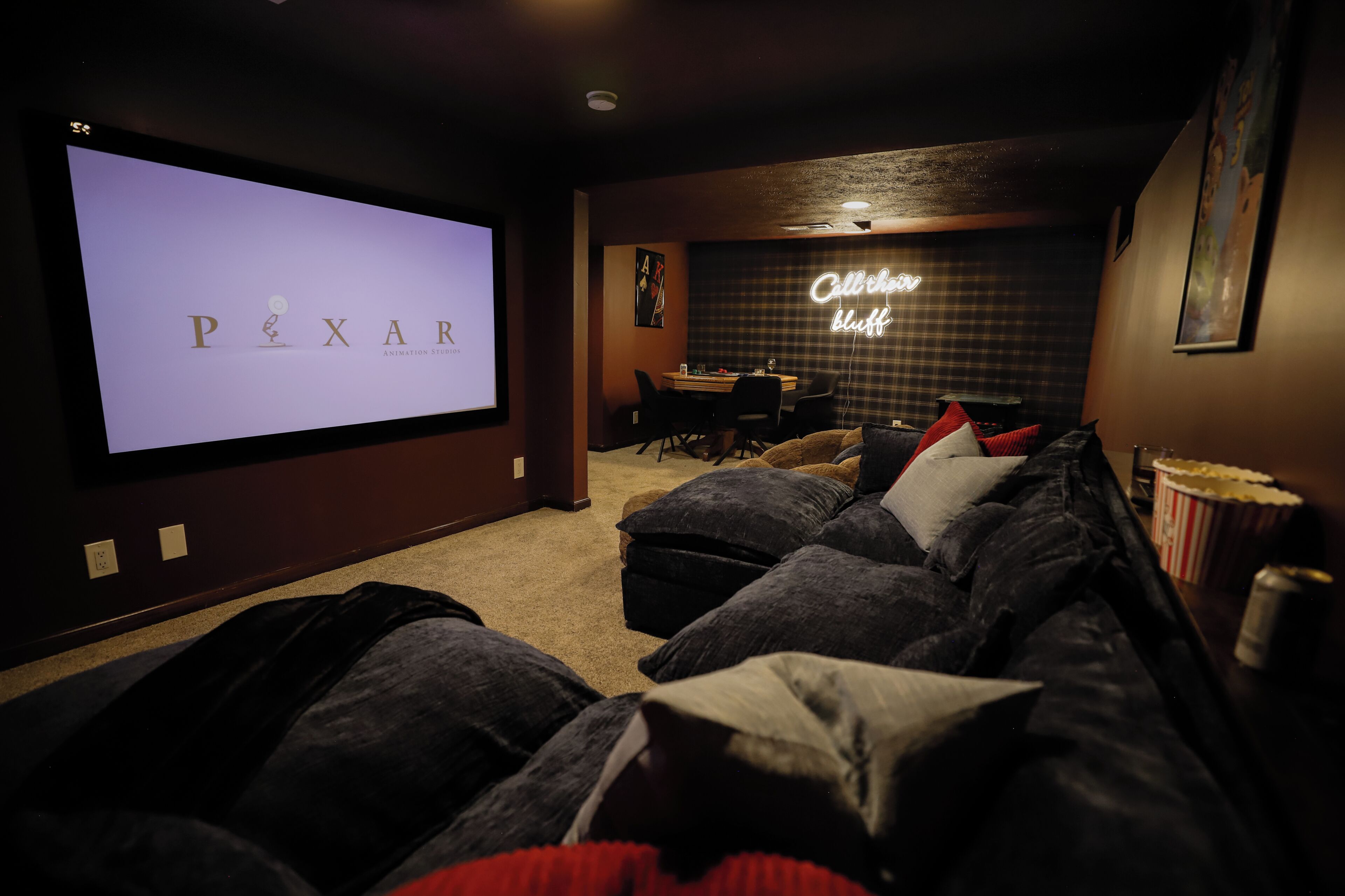A home theater room with a large screen displaying 'PIXAR ANIMATION STUDIOS' and a neon sign that reads 'Call the bluff.'
