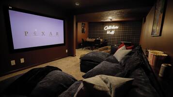 A home theater room with a large screen displaying 'PIXAR ANIMATION STUDIOS' and a neon sign that reads 'Call the bluff.'