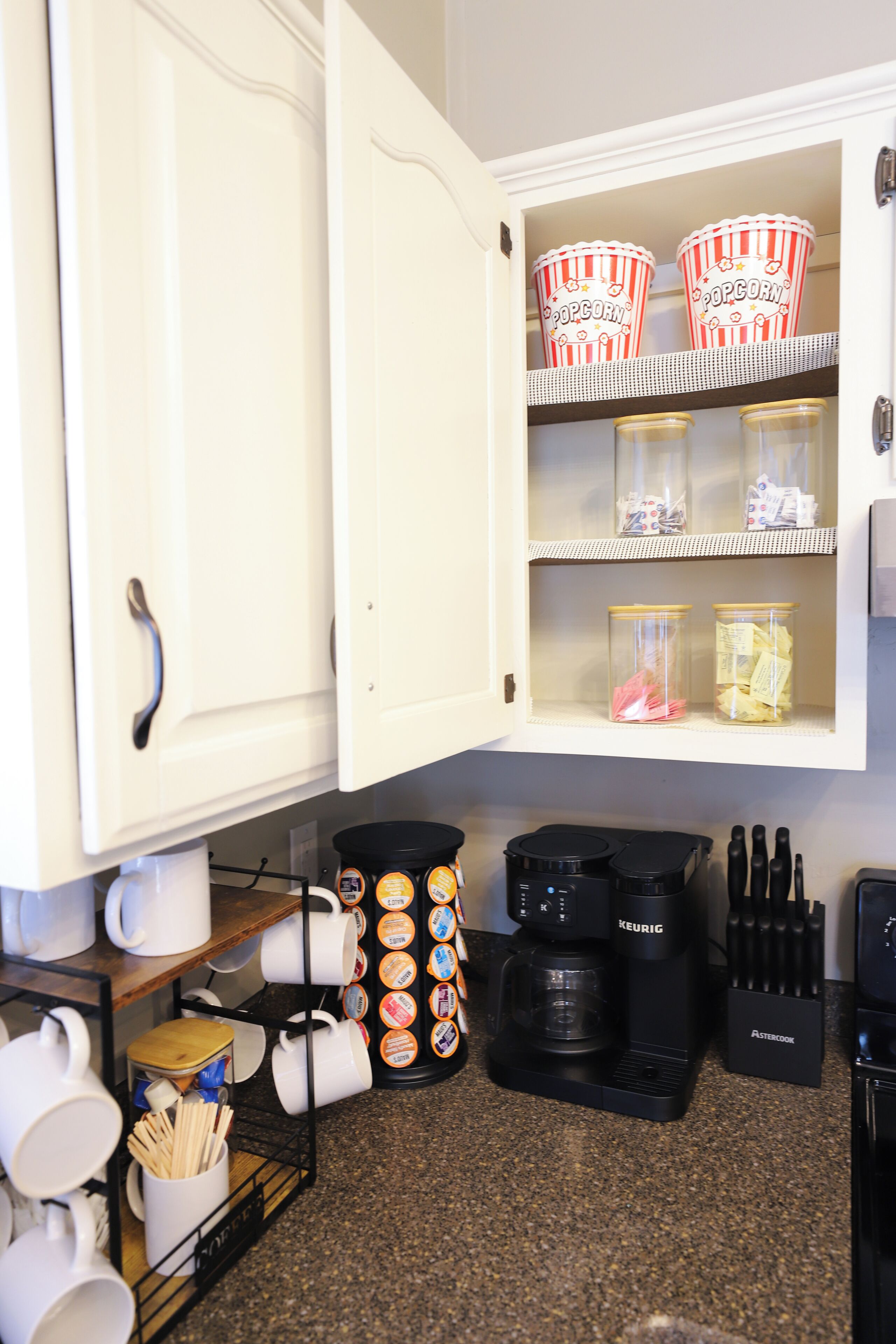 A kitchen with a coffee maker, mugs, and a popcorn container.