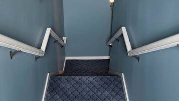 Una escalera con alfombra estampada, luces fijadas a la pared y barandilla.