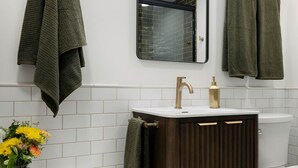 A bathroom with a white vanity, a dark wooden vanity, a white toilet, and a mirror with a black frame. - The Bloomberg at Bloomberg Suites (Chanhassen)